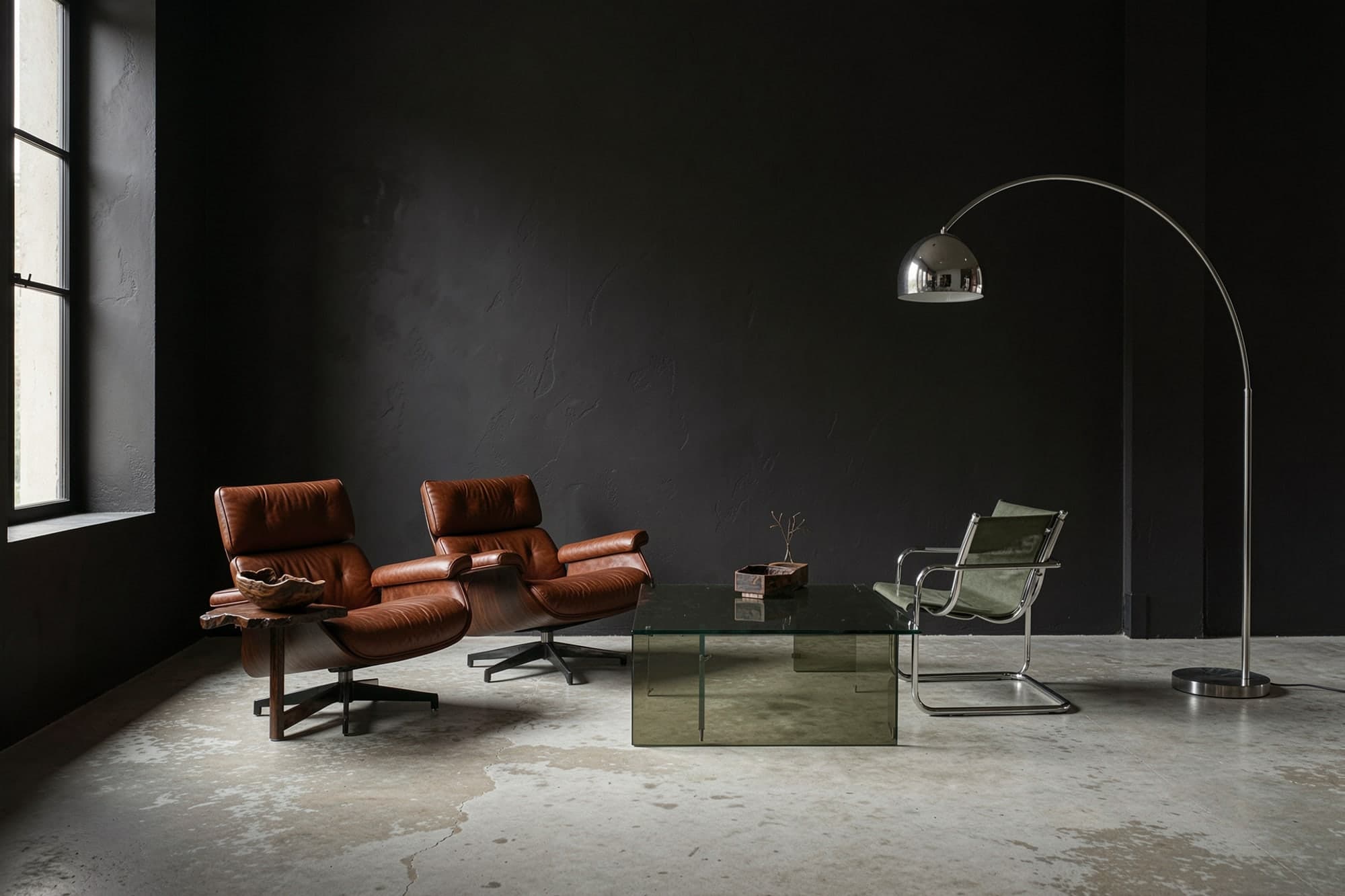 Leather lounge chairs, a glass coffee table and an arc floor lamp in a dark room